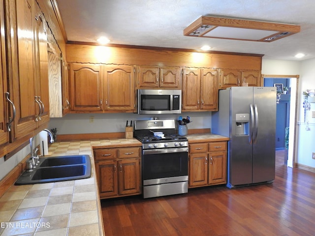 kitchen with appliances with stainless steel finishes, dark hardwood / wood-style flooring, tile countertops, and sink