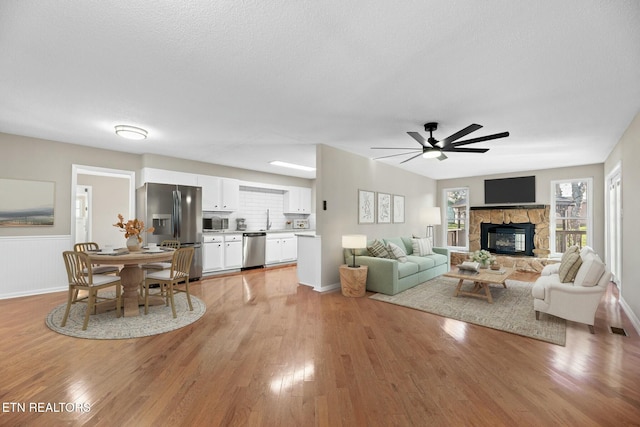 living room featuring a stone fireplace, sink, ceiling fan, light wood-type flooring, and a textured ceiling