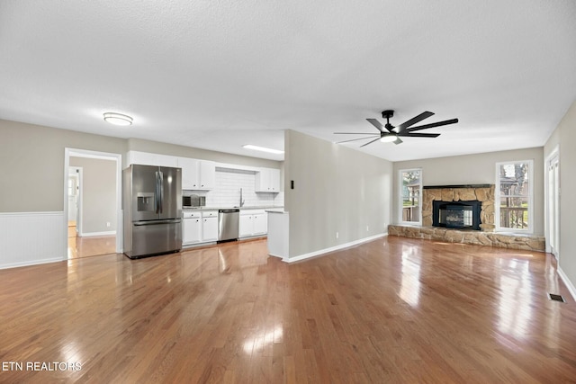 unfurnished living room featuring ceiling fan, sink, a stone fireplace, light hardwood / wood-style flooring, and a textured ceiling