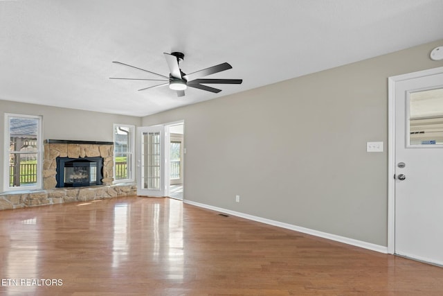 unfurnished living room with a stone fireplace, a wealth of natural light, ceiling fan, and hardwood / wood-style flooring