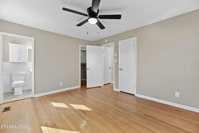 unfurnished bedroom with ensuite bathroom, ceiling fan, light hardwood / wood-style floors, and tile walls