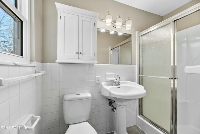 bathroom with sink, a shower with door, tile walls, and toilet