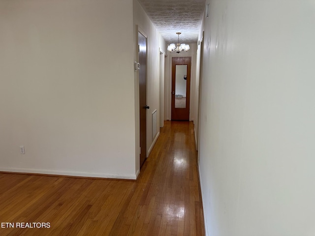 corridor with hardwood / wood-style flooring and an inviting chandelier