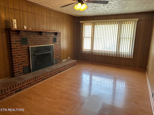 unfurnished living room featuring a brick fireplace, a textured ceiling, ceiling fan, wooden walls, and light hardwood / wood-style flooring