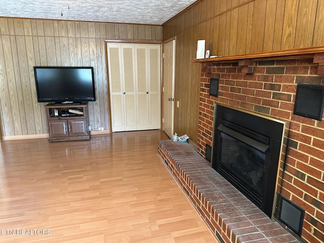 living room featuring a textured ceiling, light hardwood / wood-style floors, a brick fireplace, and wooden walls