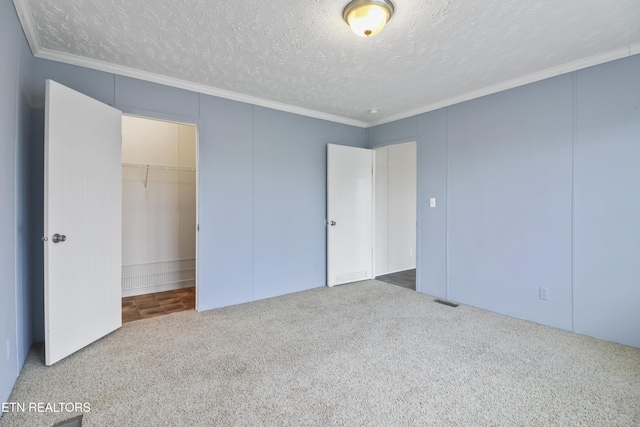 unfurnished bedroom featuring a walk in closet, carpet flooring, ornamental molding, a textured ceiling, and a closet