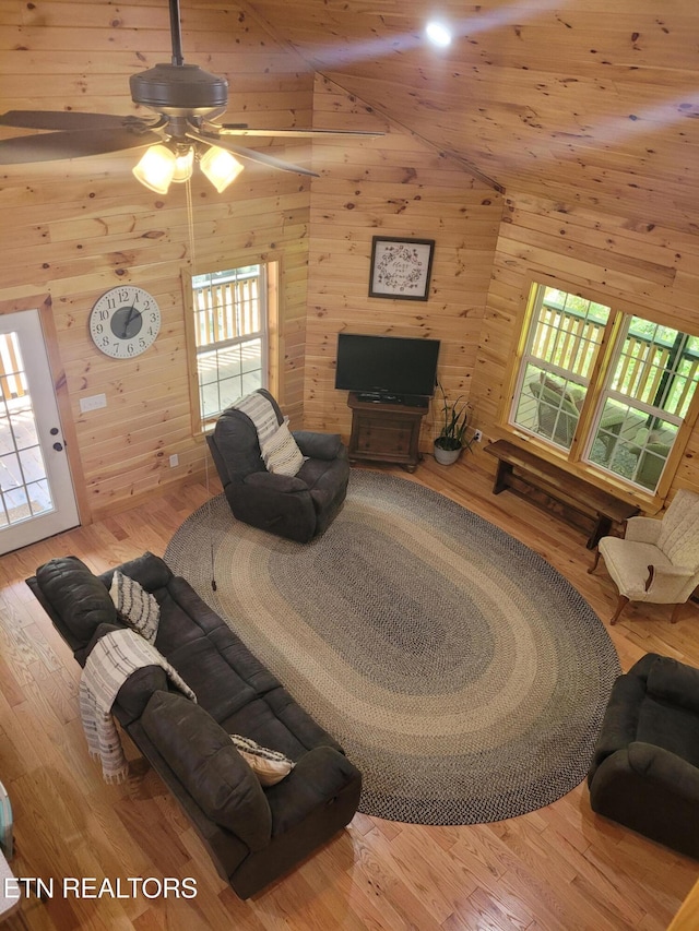 living room featuring wood-type flooring, wooden walls, and high vaulted ceiling