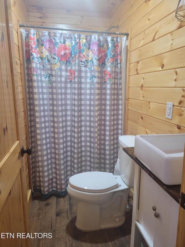 bathroom with toilet, wood-type flooring, wooden walls, and sink