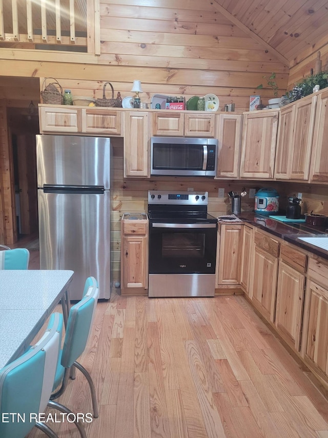 kitchen with lofted ceiling, light wood-type flooring, wood walls, and appliances with stainless steel finishes