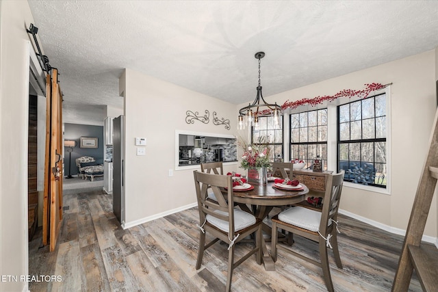 dining space featuring wood-type flooring, a barn door, and a textured ceiling