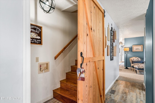 stairs with wood-type flooring, a barn door, and a textured ceiling