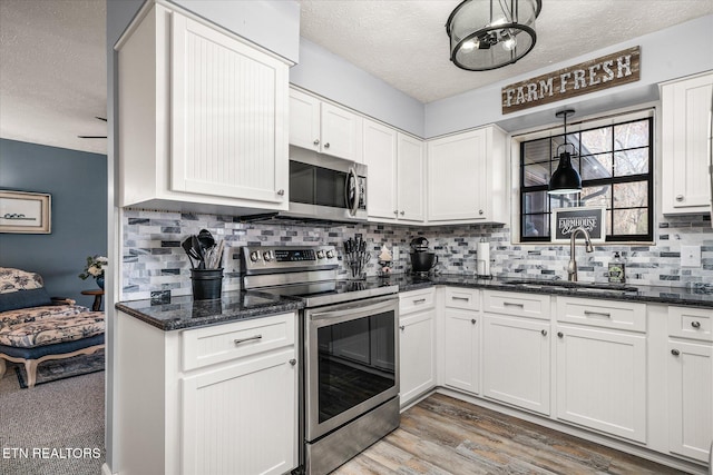 kitchen with stainless steel appliances, sink, hardwood / wood-style flooring, white cabinetry, and hanging light fixtures