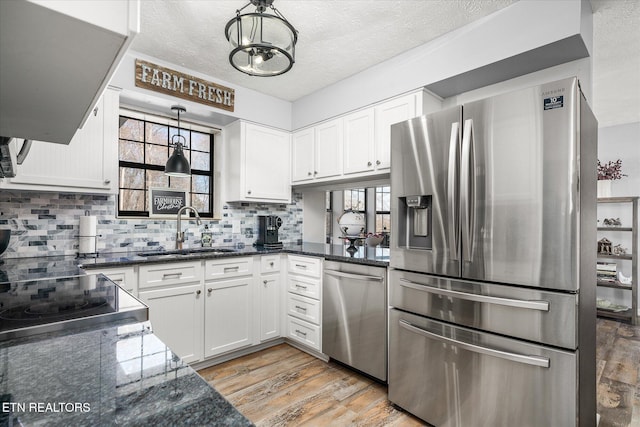 kitchen with sink, hanging light fixtures, appliances with stainless steel finishes, white cabinets, and light wood-type flooring