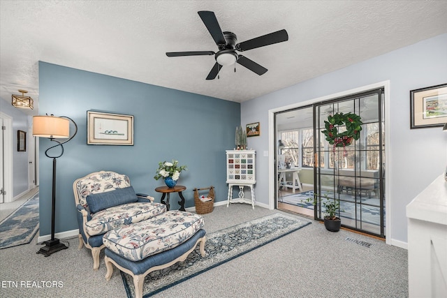 living area featuring ceiling fan, carpet floors, and a textured ceiling