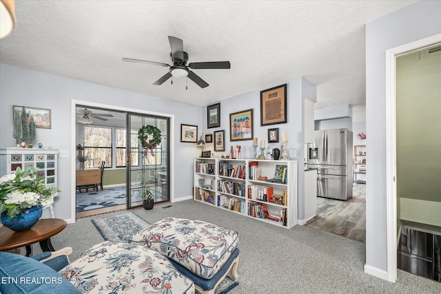 living area with carpet flooring, ceiling fan, and a textured ceiling