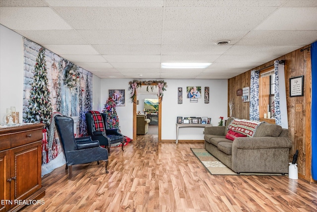 living room featuring a drop ceiling, wood walls, and light hardwood / wood-style flooring