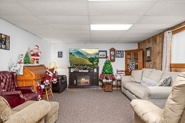 carpeted living room with a drop ceiling and wood walls