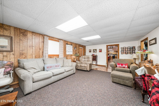 living room featuring a paneled ceiling, carpet floors, and wooden walls