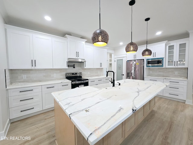 kitchen with a large island with sink, a sink, stainless steel appliances, under cabinet range hood, and light wood-type flooring