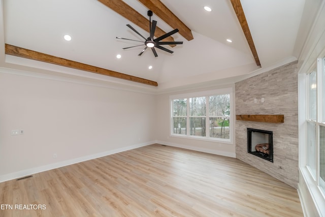 unfurnished living room with beam ceiling, wood finished floors, a stone fireplace, baseboards, and ceiling fan