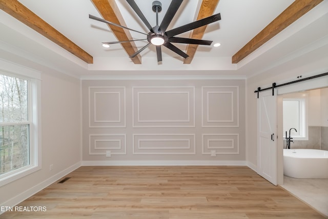 interior space with visible vents, beam ceiling, light wood-style flooring, a barn door, and baseboards