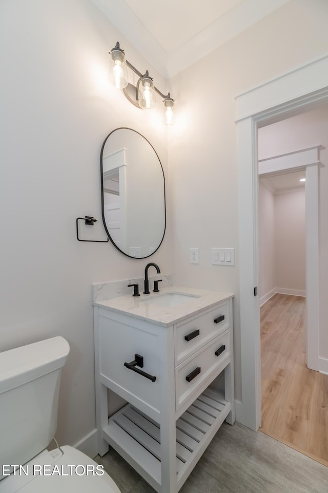 half bath featuring vanity, toilet, wood finished floors, and baseboards