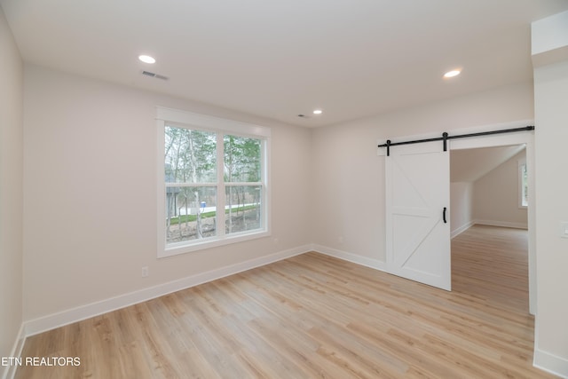 unfurnished room featuring light wood-type flooring, visible vents, a barn door, and recessed lighting