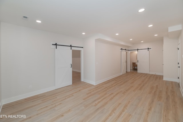 unfurnished room with a barn door, light wood-style flooring, recessed lighting, and baseboards