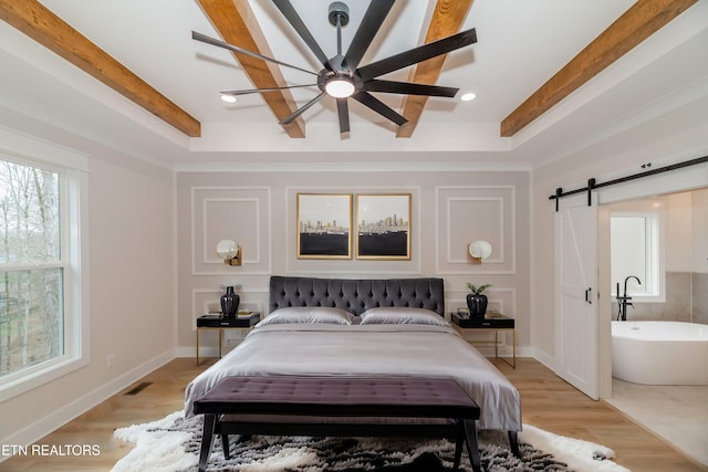 bedroom featuring visible vents, beamed ceiling, light wood-style floors, and a barn door