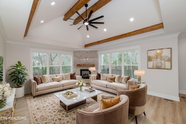 living area featuring a stone fireplace, beamed ceiling, light wood-style floors, and a healthy amount of sunlight