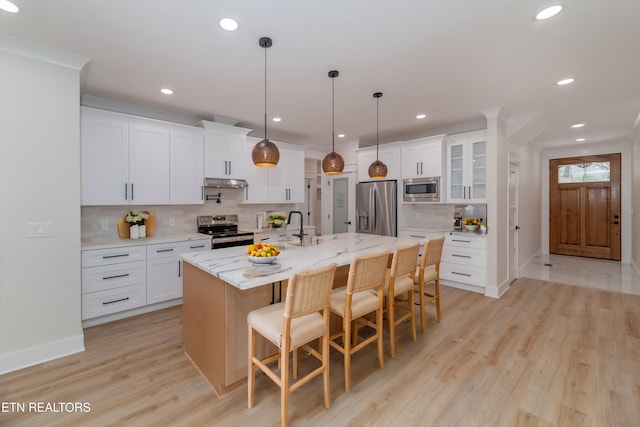 kitchen with light wood finished floors, a breakfast bar, under cabinet range hood, appliances with stainless steel finishes, and white cabinetry