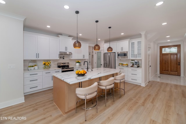 kitchen featuring a kitchen bar, light wood-type flooring, under cabinet range hood, backsplash, and stainless steel appliances