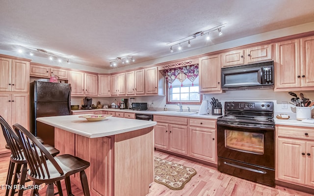 kitchen with rail lighting, sink, black appliances, a kitchen island, and a breakfast bar area