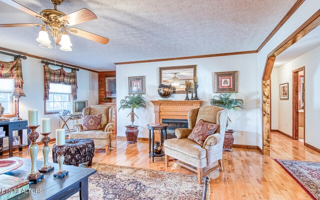 living room with a textured ceiling, light wood-type flooring, ceiling fan, and crown molding