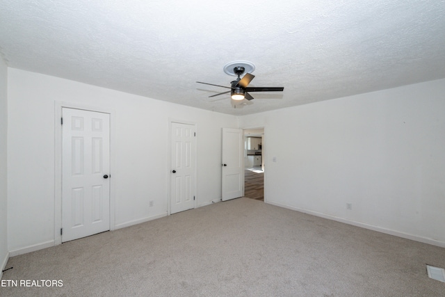 unfurnished bedroom with a textured ceiling, light colored carpet, and ceiling fan