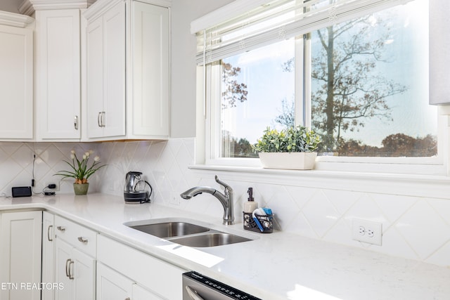 kitchen with tasteful backsplash, white cabinetry, sink, and light stone countertops