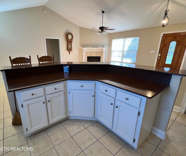 kitchen with ceiling fan, a tile fireplace, pendant lighting, white cabinetry, and light tile patterned flooring