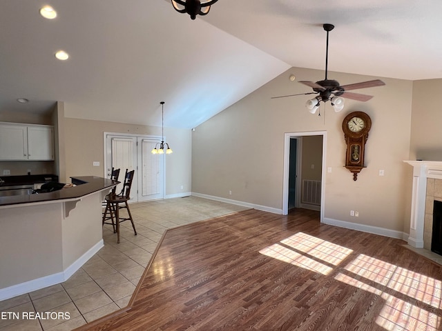 unfurnished living room featuring light wood-type flooring, ceiling fan, sink, lofted ceiling, and a tiled fireplace