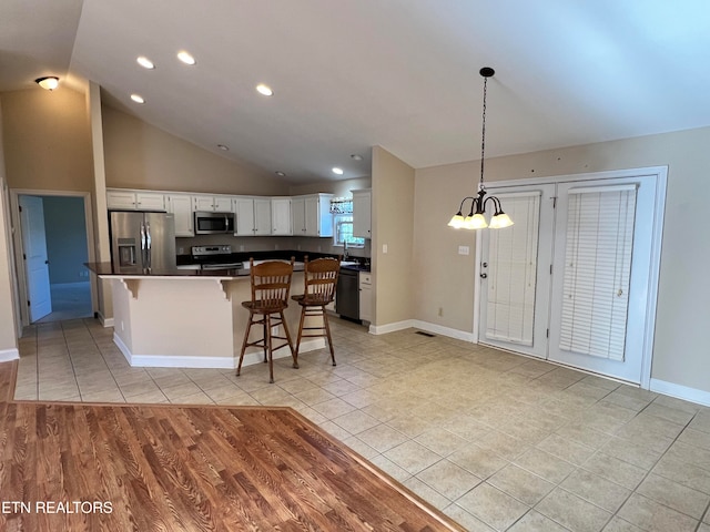 kitchen with stainless steel appliances, vaulted ceiling, decorative light fixtures, white cabinets, and a breakfast bar area