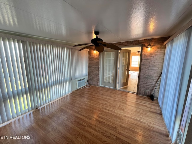 unfurnished living room featuring a textured ceiling, hardwood / wood-style flooring, ceiling fan, and brick wall