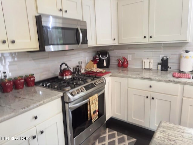 kitchen with white cabinets, decorative backsplash, light stone countertops, and appliances with stainless steel finishes