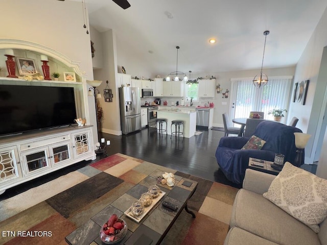 living room featuring ceiling fan with notable chandelier, vaulted ceiling, and dark wood-type flooring