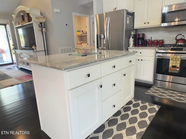 kitchen featuring stainless steel appliances, a kitchen island, light stone counters, dark hardwood / wood-style floors, and white cabinets