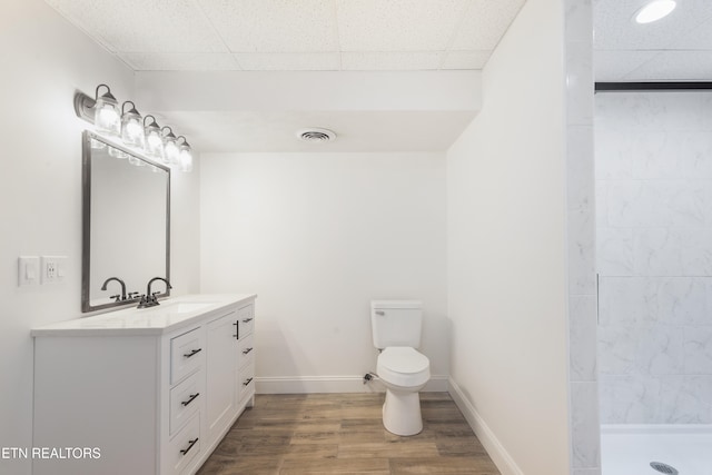 bathroom featuring hardwood / wood-style flooring, a paneled ceiling, tiled shower, vanity, and toilet