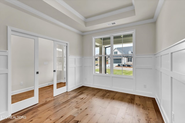 interior space featuring a raised ceiling, french doors, ornamental molding, and light wood-type flooring