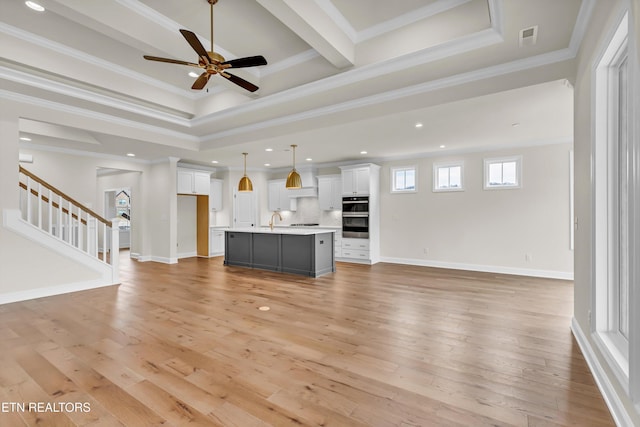 unfurnished living room featuring light wood-type flooring, a tray ceiling, ceiling fan, crown molding, and sink