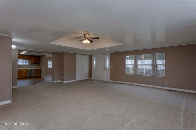 unfurnished living room featuring ceiling fan, light colored carpet, and a tray ceiling