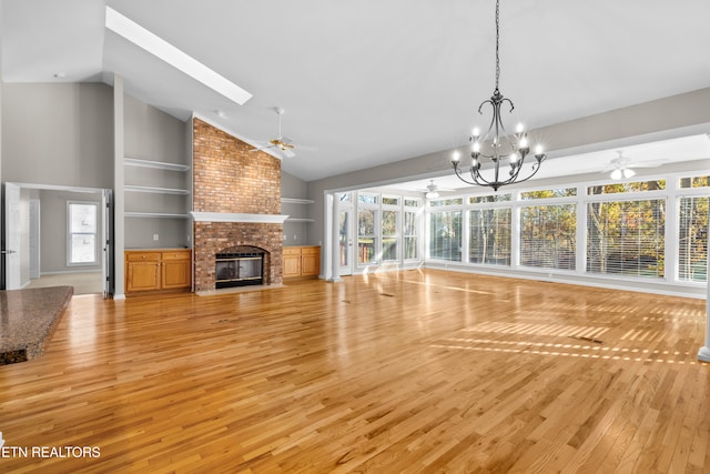 unfurnished living room featuring a fireplace, ceiling fan with notable chandelier, high vaulted ceiling, and light hardwood / wood-style flooring