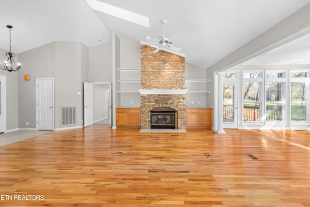 unfurnished living room with a fireplace, high vaulted ceiling, a skylight, and light hardwood / wood-style flooring