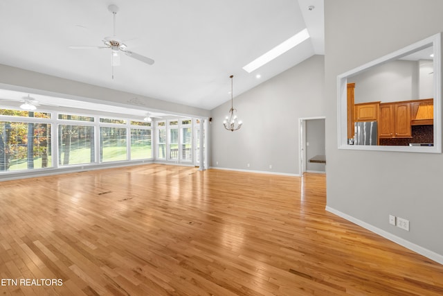 unfurnished living room featuring ceiling fan with notable chandelier, light hardwood / wood-style floors, high vaulted ceiling, and a skylight